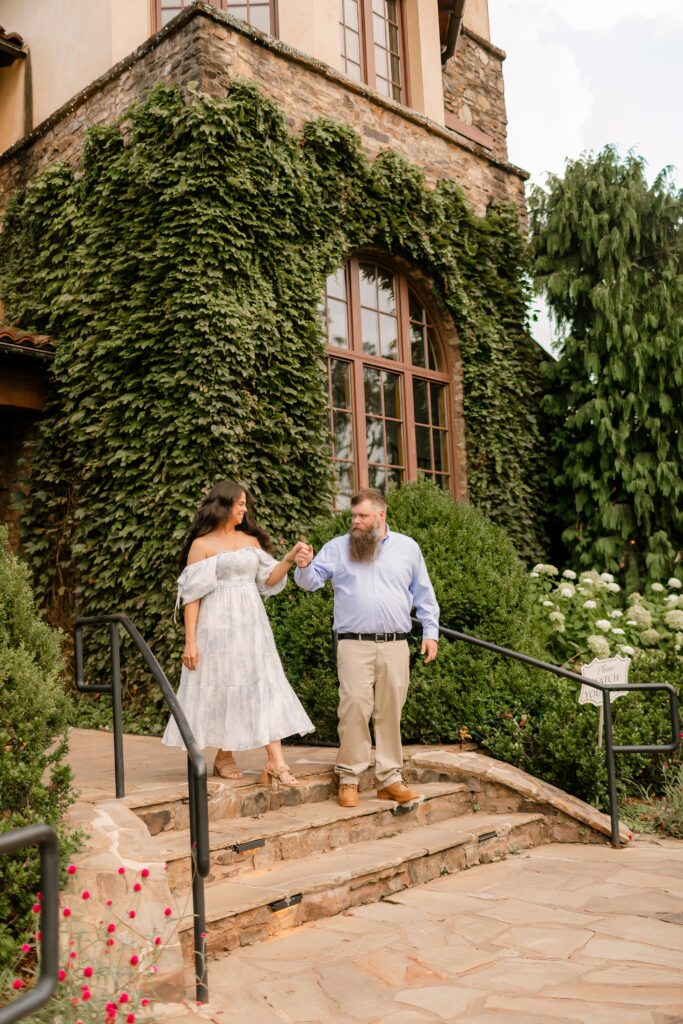 Couple walking hand in hand on stone steps outside an ivy-covered building