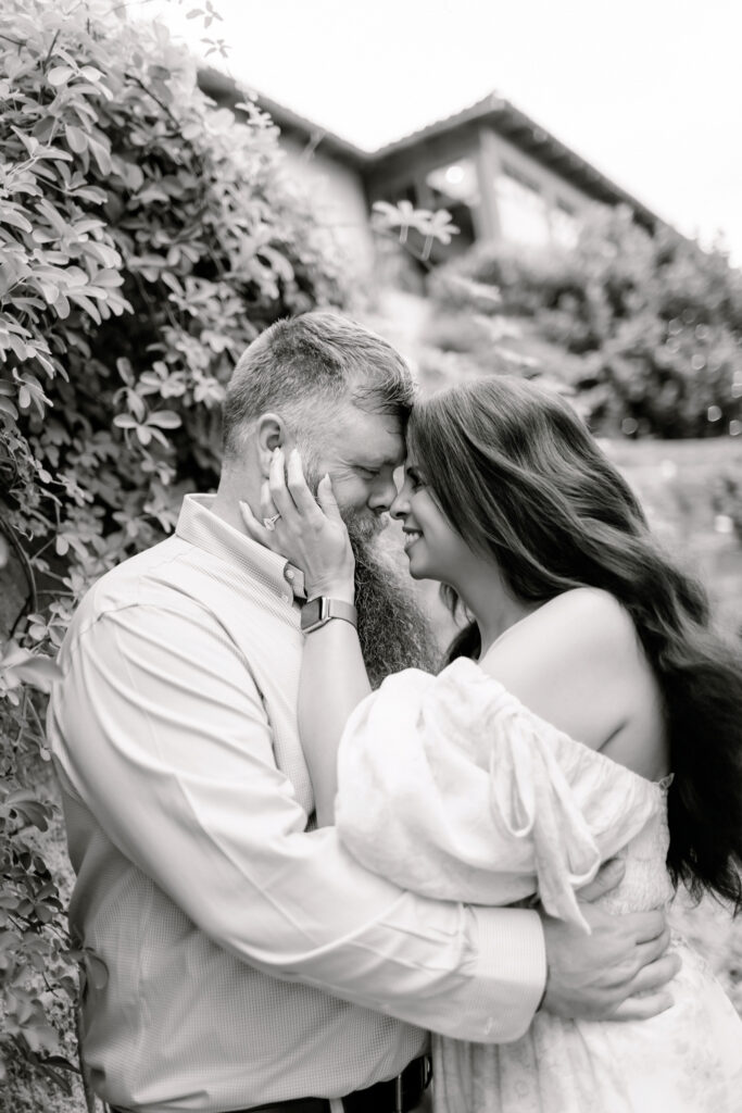 Black and white portrait of a couple embracing closely outdoors, foreheads touching in an intimate moment