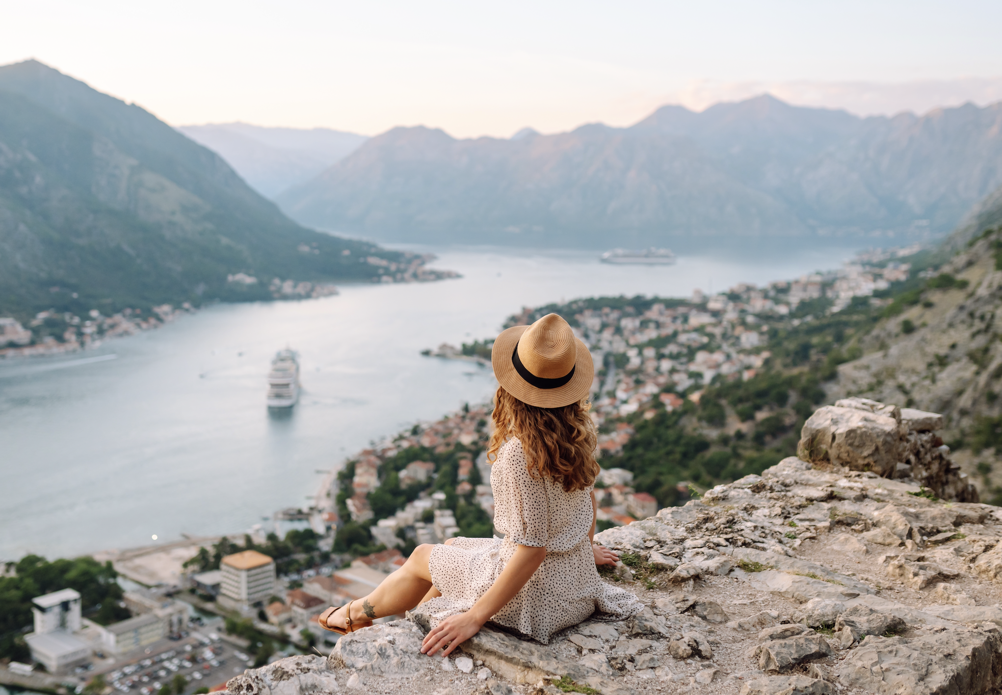 Woman sitting alone on a mountain cliff overlooking a coastal city, symbolizing independence and finding clarity in her own life.